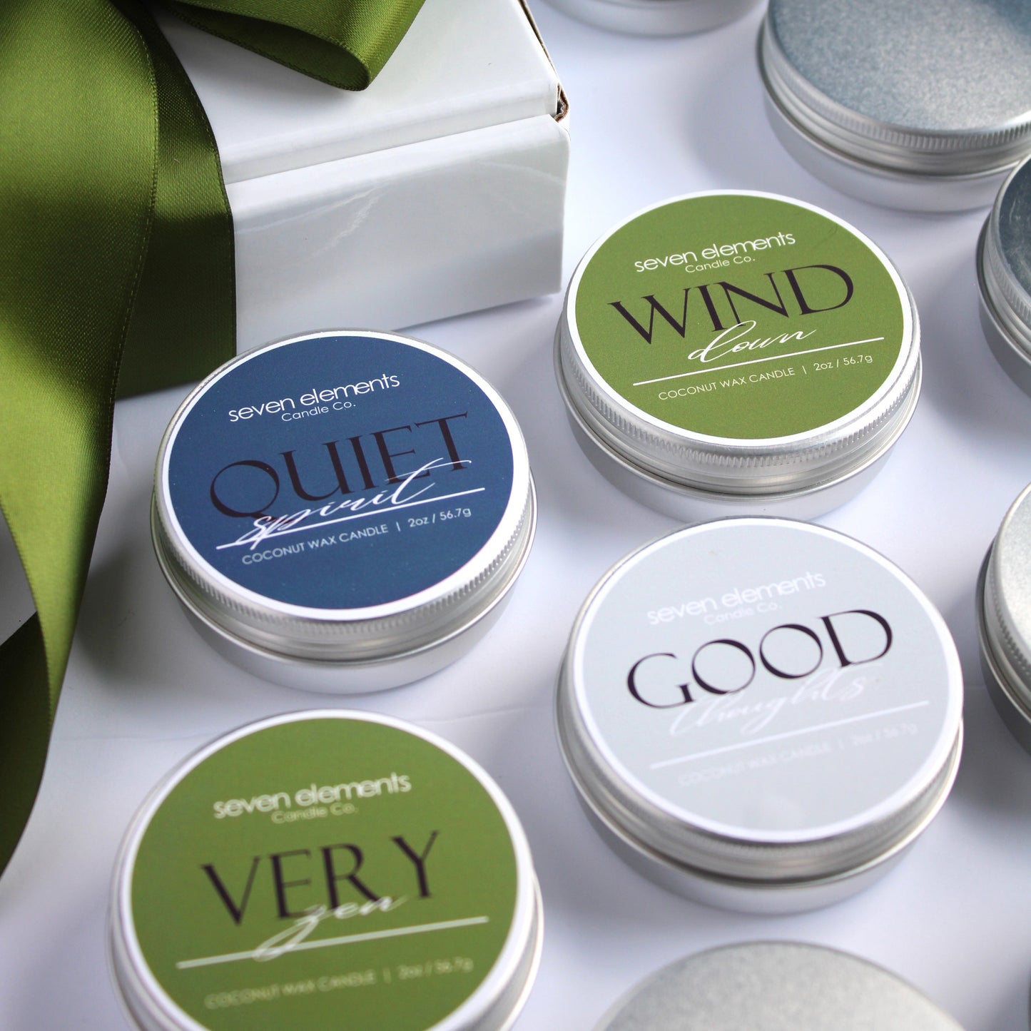 Set of small containers with lids, some labeled, on a white surface with a green ribbon.