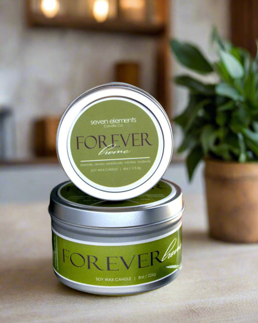 Green candle in a tin with 'Forever' label on a wooden surface, blurred background