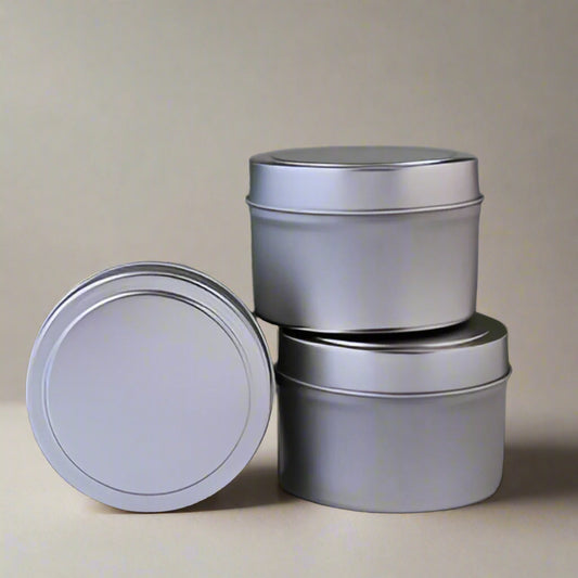 Three metallic tin containers with lids on a white surface against a green background