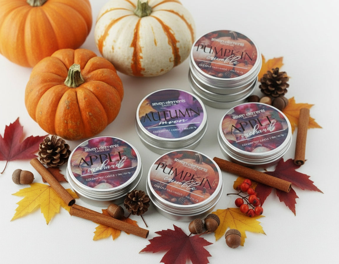 Stacks of Seven Elements candles with autumn-themed labels on a white surface with pumpkins and leaves.