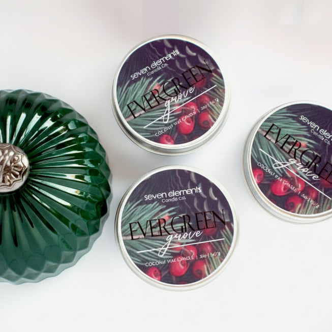 Three tins of Seven Elements Candle Co. 'Evergreen Grove' candles on a white background.