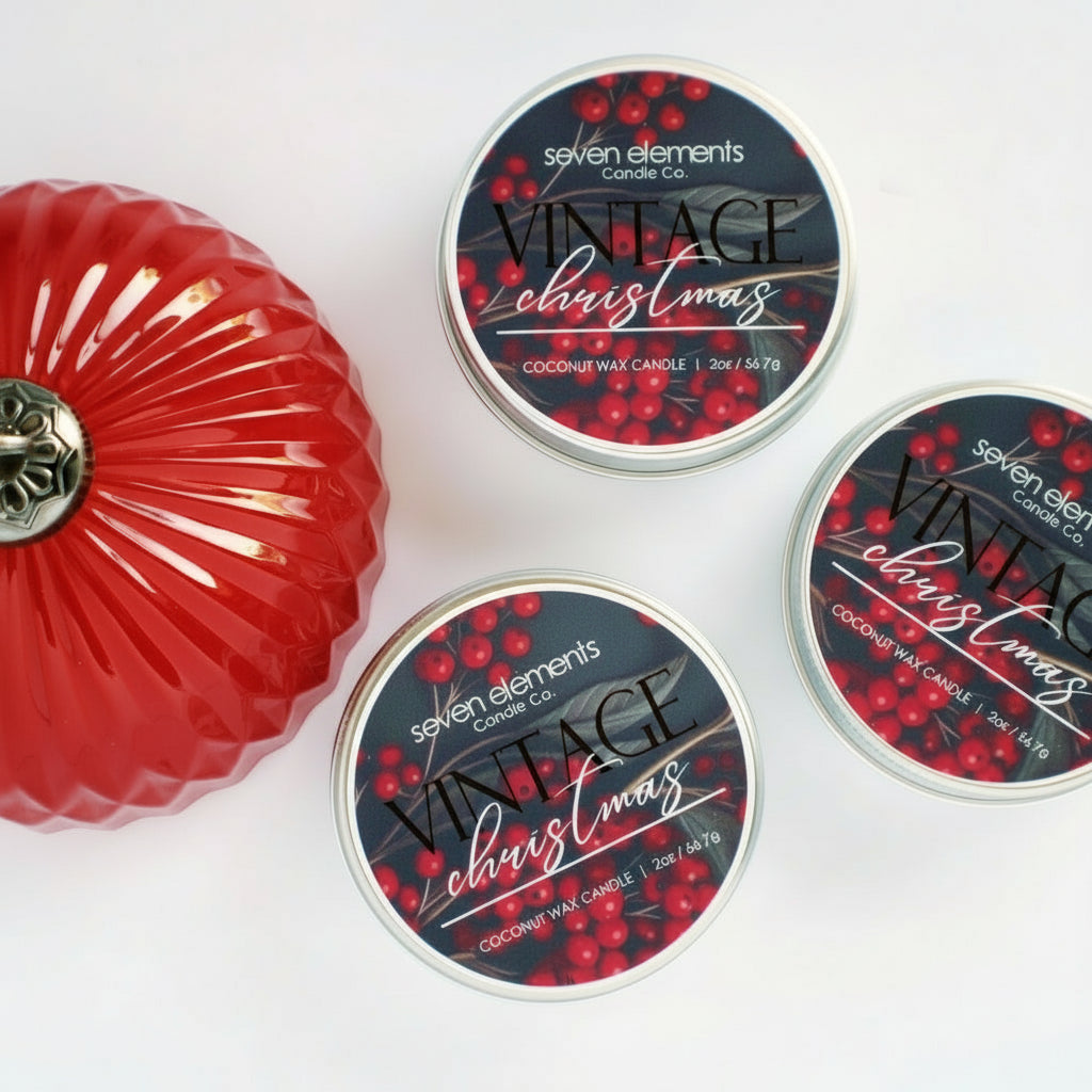 Three 'Vintage Christmas' candles from Seven Elements Candle Co. on a white background with a red decorative item.